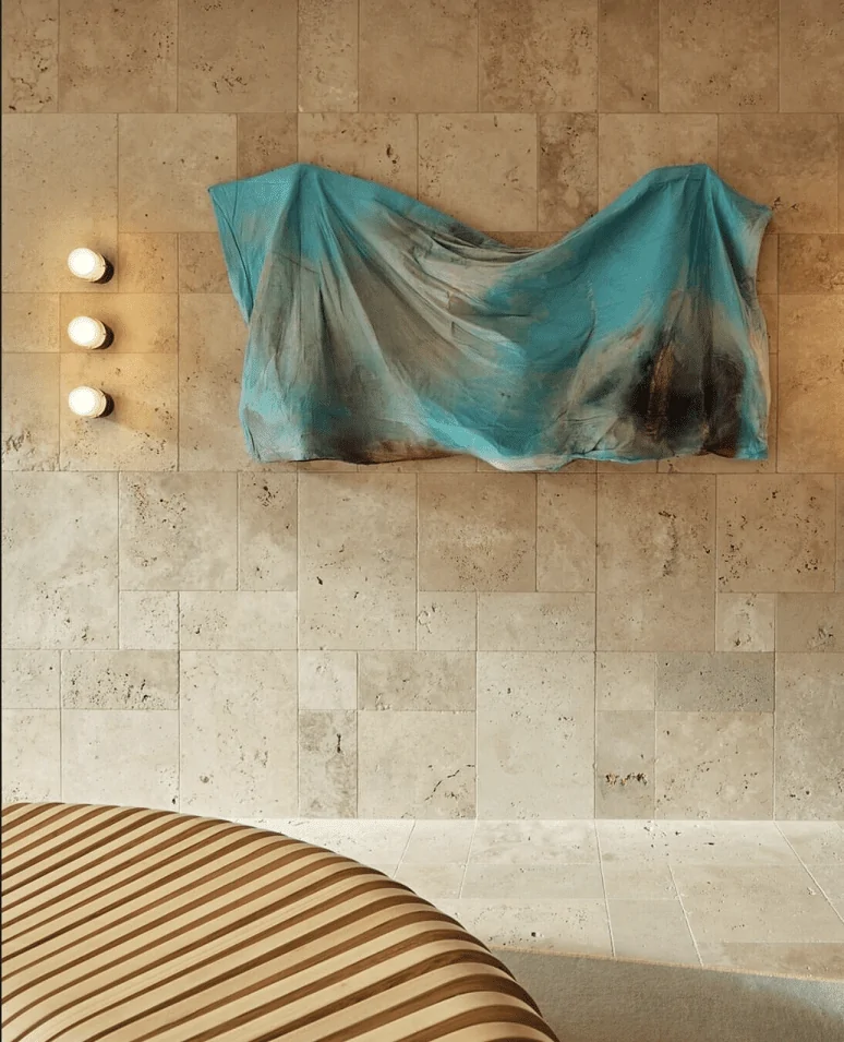 A contemporary interior with a travertine tile wall, accent lighting, and a draped blue fabric.