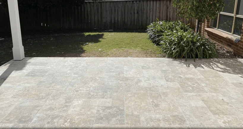 A modern outdoor patio with travertine pavers leading to a small lawn